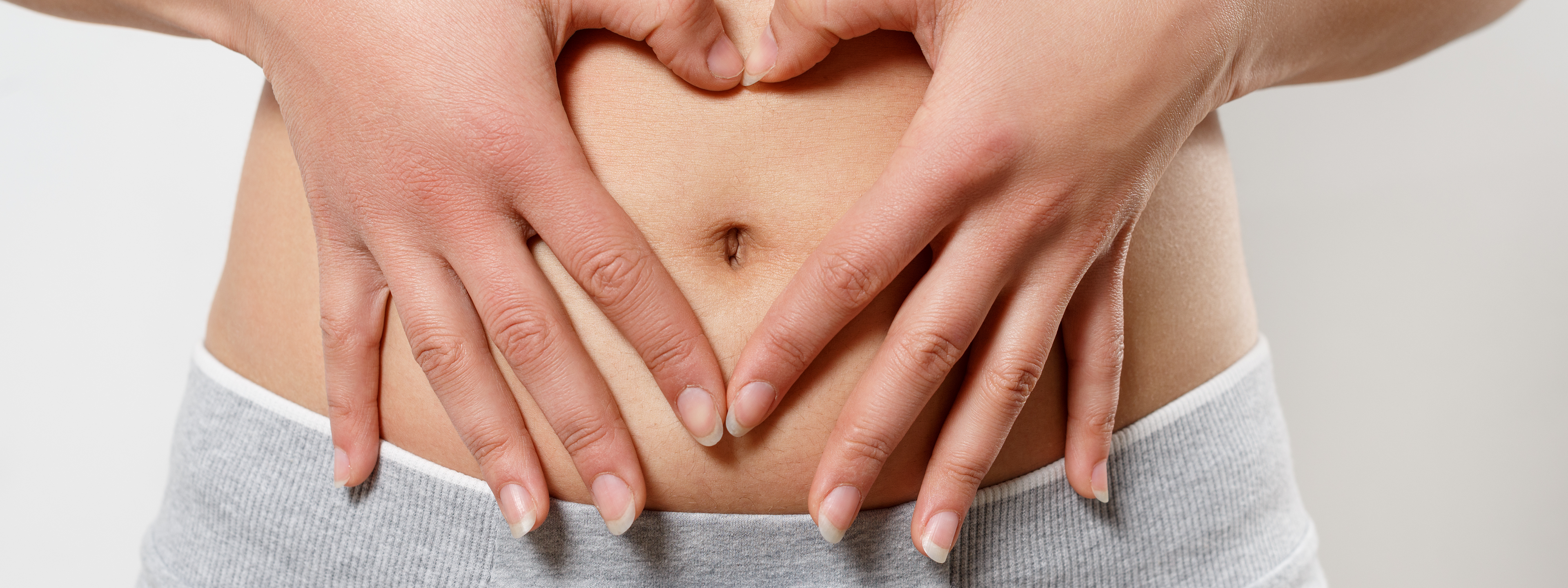 Heart-shaped hands on bare stomach, symbolizing women's health and care.
