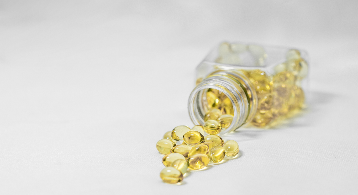 Clear softgel capsules spilling from a bottle on a white surface.