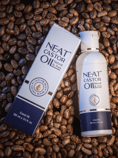 Neat Castor Oil 100% Pure Cold-Pressed bottle and box on raw castor beans. Best cold-pressed castor oil for hair, skin, and nail care.